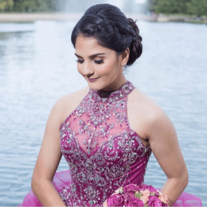 A woman in a purple Quinceanera gown with a matching hairstyle, holding a bouquet