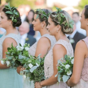 A group of women standing next to each other holding bouquets with a floral design, surrounded by decorations for a Quinceanera celebration.
