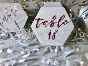 A table number surrounded by confetti and streamers, with Quinceanera party favors in Pantone colors.