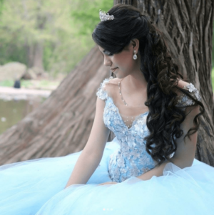 A woman in a Quinceanera gown sitting under a tree
