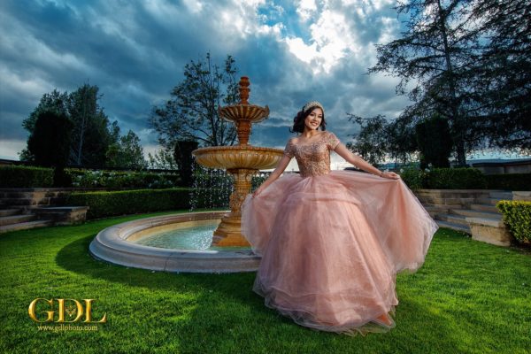 A nature Quinceañera, a woman in a pink dress sitting in front of a fountain