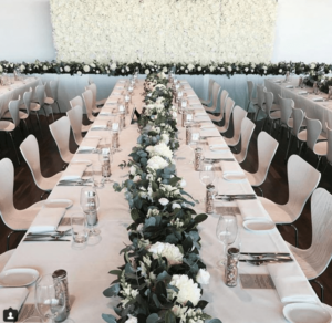 A Quinceanera function hall decorated in Pantone colors. A long table is set with white flowers and greenery.