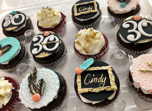 A tray of Quinceanera-themed cupcakes decorated with gold and black frosting