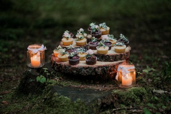 Candles in the woods accompanying a Quinceanera celebration, with cupcakes placed on a tree stump and adorned with candles.