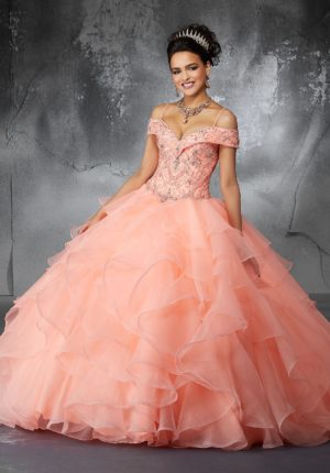 A woman in a pink princess neck gown posing for a picture at a Quinceanera celebration