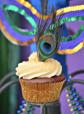 A Quinceanera themed cupcake topped with a peacock feather, decorated with buttercream resembling Brazilian Carnival