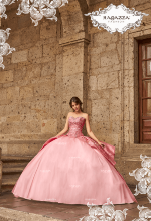 A woman in a pink gown Quinceañera dress standing in front of a building.