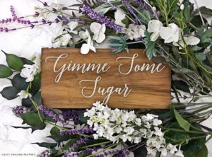 A close up of a wooden sign with lilac floral design and flowers.