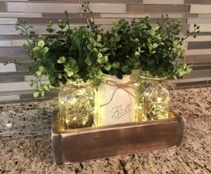 Quinceanera rustic table centerpiece ideas. A table with three mason jars filled with plants on a counter.