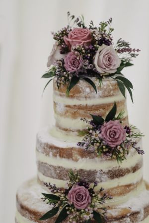 A Quinceanera-themed naked wedding cake featuring three tiers with flowers on top