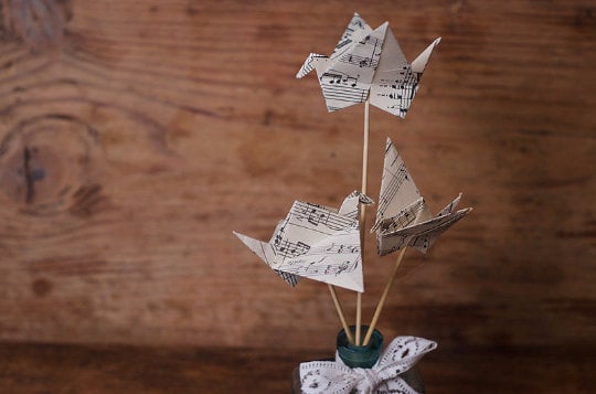 An origami Quinceañera theme, featuring a vase filled with paper birds on top of a wooden table.