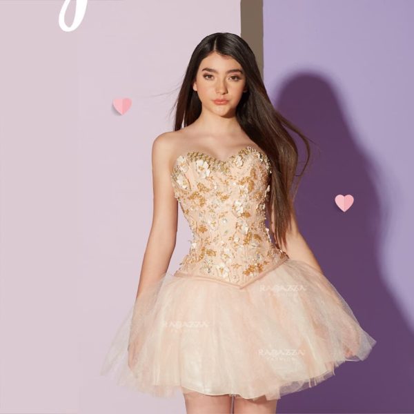 Quinceanera image: A woman in a short cocktail dress standing in front of a wall
