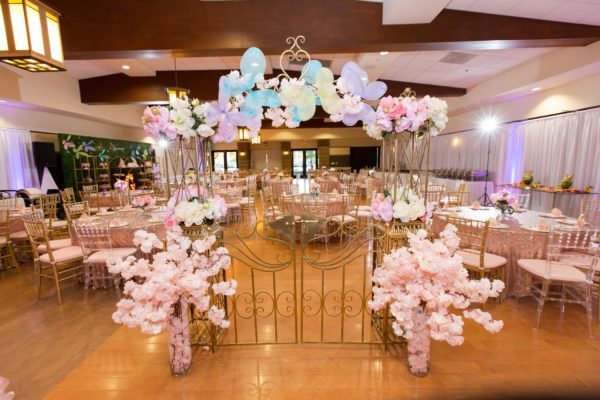 A Quinceanera function hall filled with lots of tables and chairs showcasing a beautiful centerpiece.