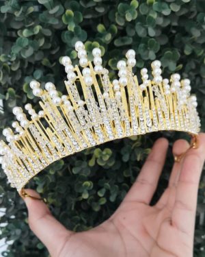 A hand holding a gold and white pearl crown, with a Quinceanera jewellery headpiece