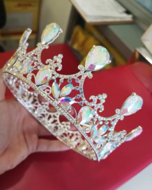 A person holding a silver crown on top of a table with Quinceanera jewellery