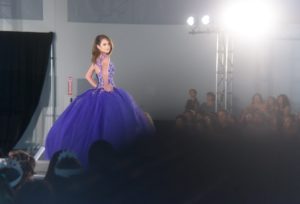A beautiful Quinceanera girl wearing a purple dress walking down a runway