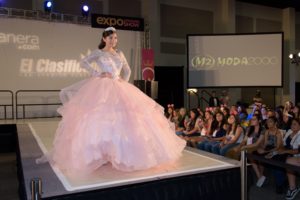 Fashion show gown: A woman in a pink dress walking on a runway at a Quinceanera fashion show.