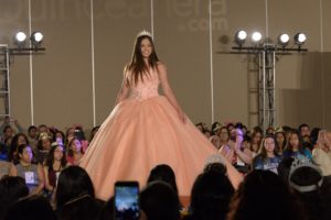 A Quinceanera fashion model in a pink haute couture dress walking down a runway