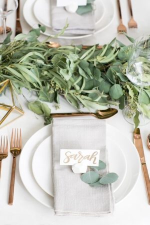 A Quinceanera table set with white plates, silverware, and greenery decorations