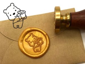 A Quinceanera-themed wax seal with a drawing of a teddy bear on it.