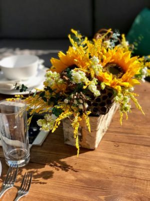 A Quinceanera-themed image featuring a floral bouquet and a wooden table topped with a vase filled with sunflowers