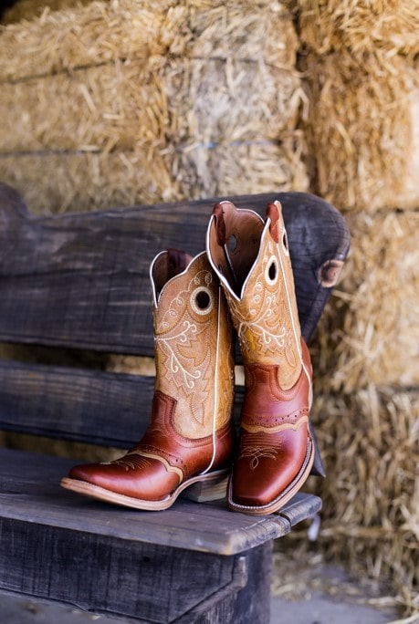 A pair of cowboy boots sitting on a bench at an outdoor Quinceañera celebration.