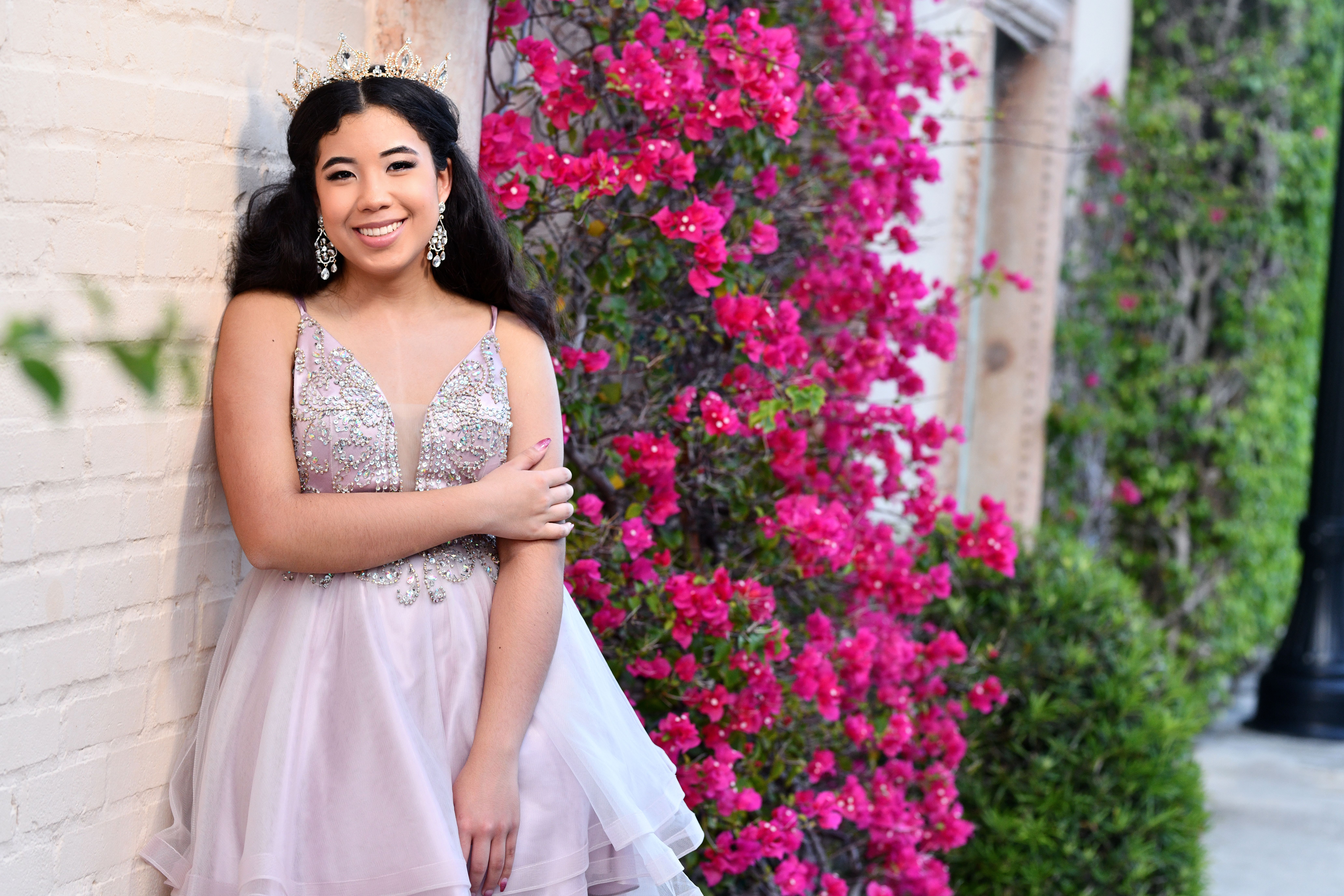 A woman wearing a gown Quinceañera standing in front of a wall with pink flowers.
