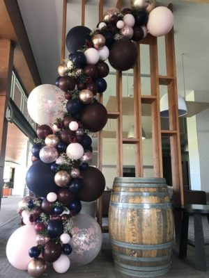 Quinceanera decoration with rose gold and burgundy balloon garland, featuring a bunch of balloons and a barrel of wine