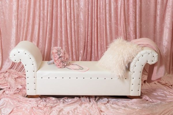 A Quinceanera-themed image featuring a white bench sitting on top of a pink blanket beside a couch sofa.