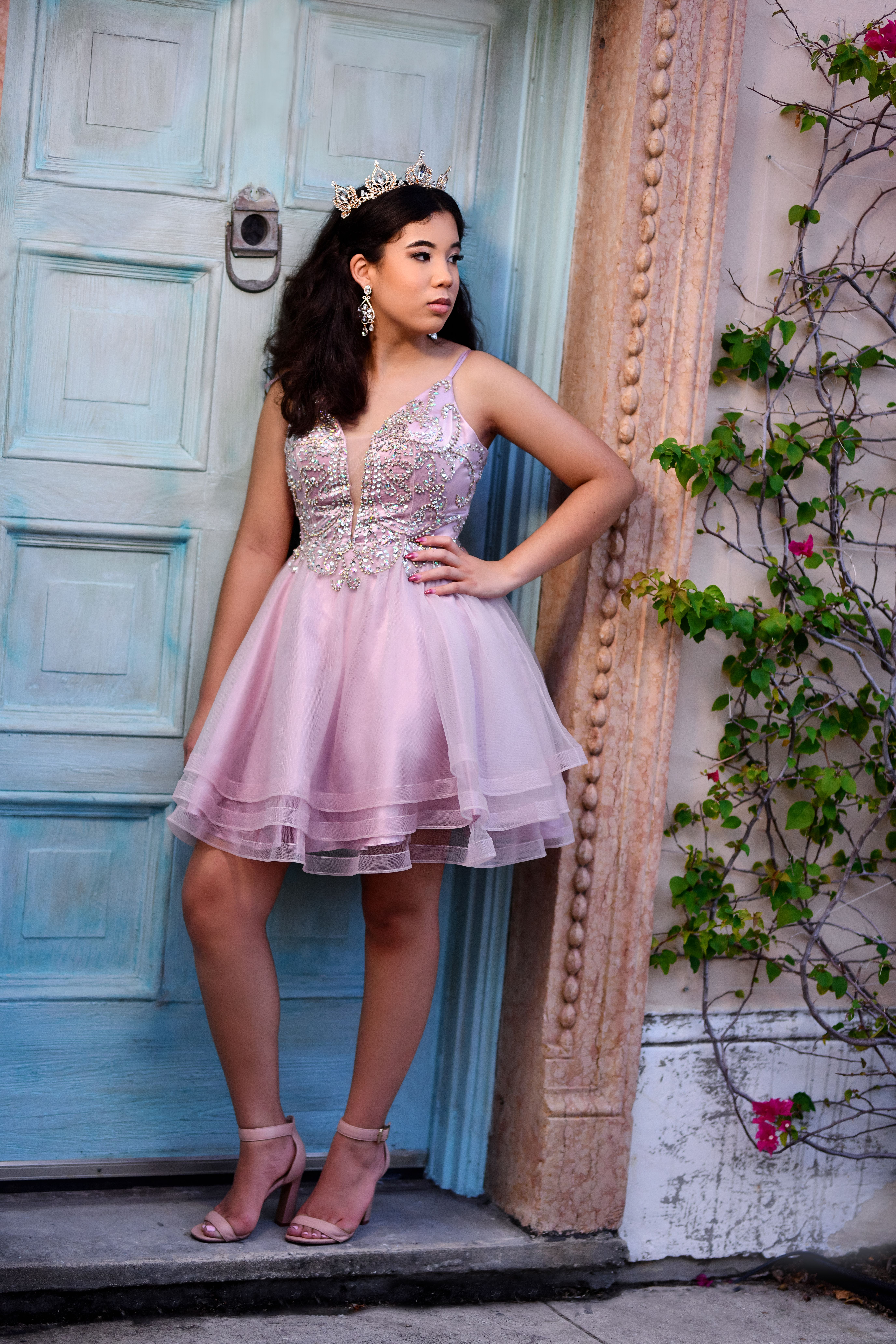 A Quinceanera in a cocktail dress standing in front of a blue door
