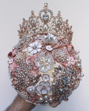 A man holding a bouquet with a crown on top of it, featuring a brooch