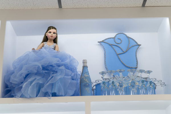 Photograph of Última muñeca, a doll in a blue dress sitting on a shelf at a Quinceanera celebration.