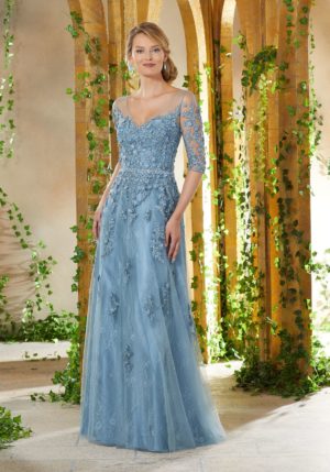 Quinceanera image: A woman in a blue dress standing in a courtyard, wearing an MGNY mother of the bride dress.