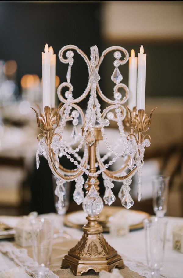 A Quinceanera-themed gold candelab with crystal candles resting on a table, serving as a candle holder centrepiece