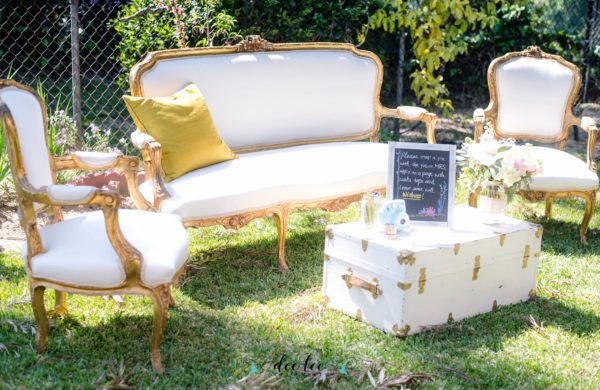 A group of white couches sitting on top of a lush green field with a Victorian era chair.
