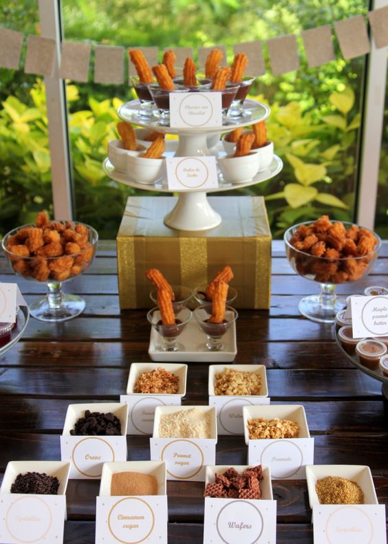 A colorful Quinceanera churro station, featuring a table topped with lots of different types of food.