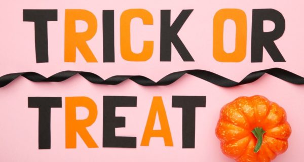 A Quinceanera sign that says trick or treat next to a pumpkin, with orange font