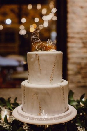 A white Quinceanera cake with gold decoration on top and a moon design