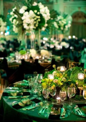 A table set for a formal Quinceanera dinner in an emerald theme, with candles and flowers