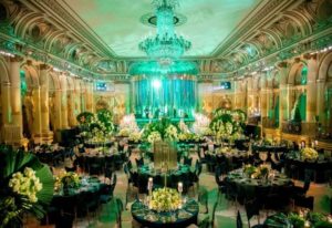 A Quinceanera celebration with an emerald city theme. The room is filled with lots of tables and chairs adorned with beautiful floral designs.
