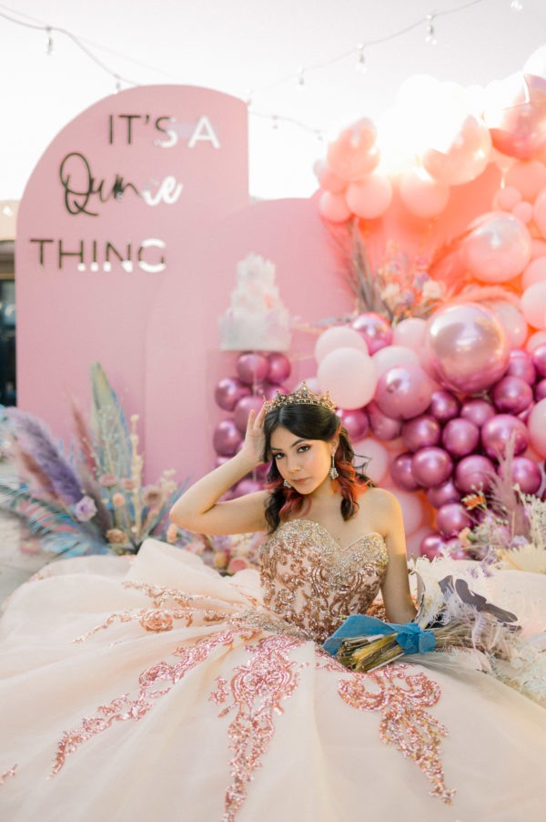 A beautiful woman in a Quinceanera dress sitting in front of balloons at a Quinceanera party.
