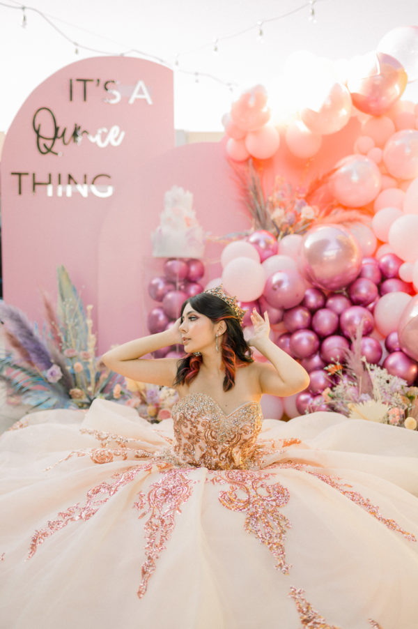 Pink flower Quinceanera: a woman in a ball gown sitting in front of balloons