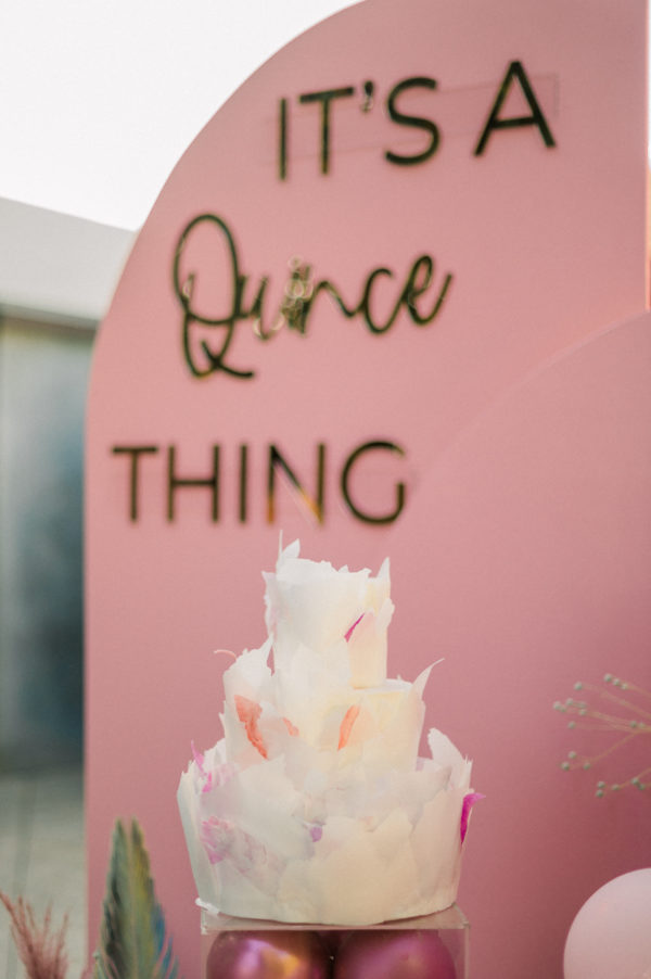 Cake decorating, a Quinceanera cake sitting on top of a table next to a sign