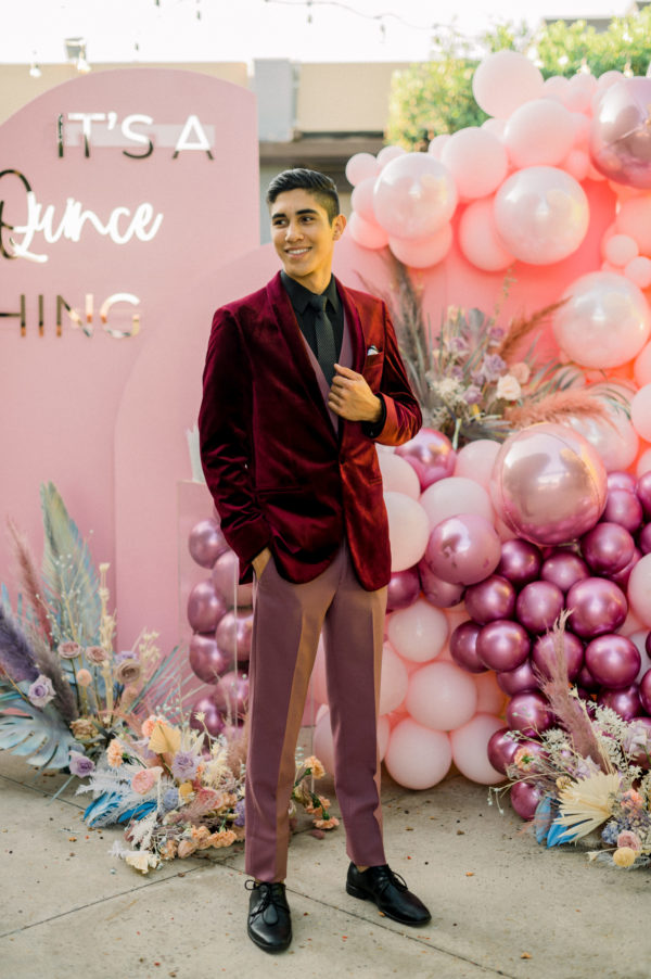 A girl Quinceañera standing in front of a wall of balloons, with a man standing alongside