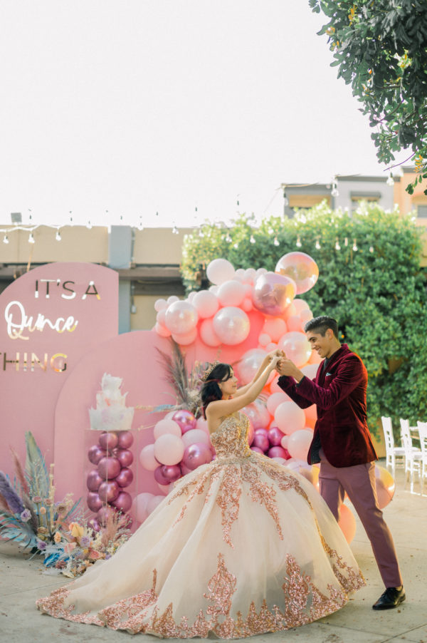 A Quinceanera celebration with rose gold chambelanes and Quinceañera dresses, featuring a man and a woman dancing in front of balloons