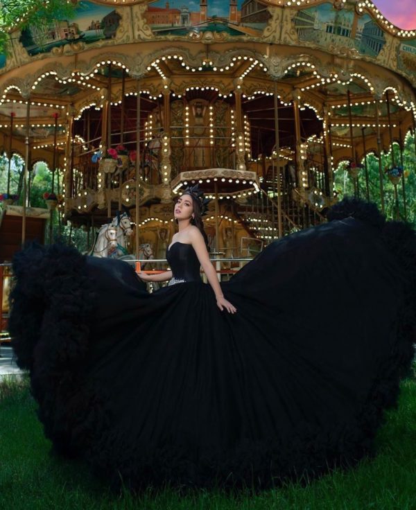 A woman in a black dress standing in front of a carousel, surrounded by Quinceañera dresses at Bosque de Chapultepec.