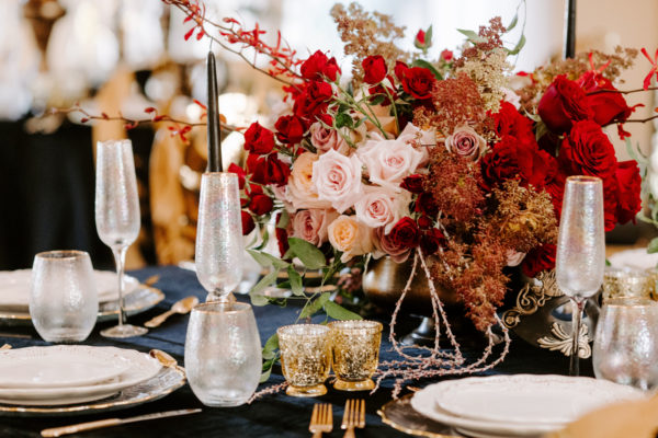 A Quinceanera table set for a formal dinner with a floral centerpiece, featuring red and white flowers.