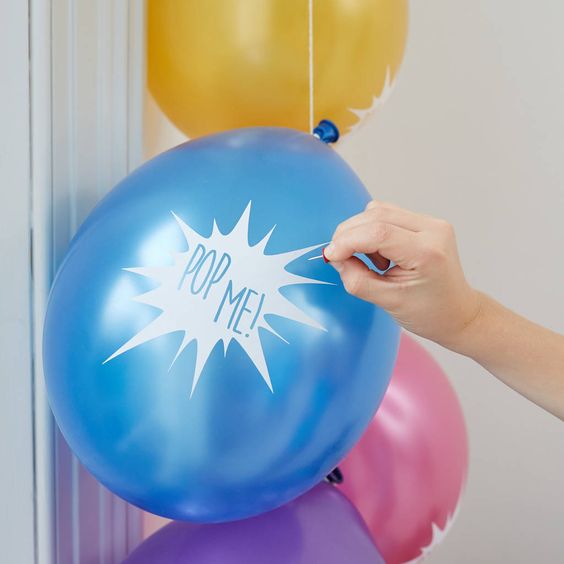 A person holding a pair of scissors above a bunch of balloons, bursting secrets