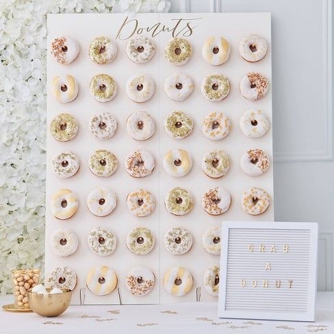 A Quinceanera party display featuring a donut wall with a table filled with lots of Quinceanera-themed doughnuts, next to a sign
