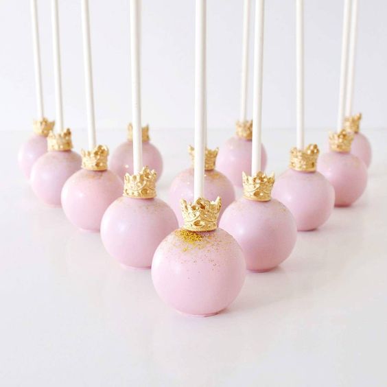 Christmas ornament cake with a bunch of Quinceanera-themed cake pops decorated with gold crowns.